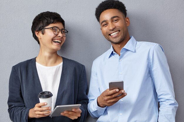 Compañeros de trabajo positivos de raza mixta trabajan con tabletas modernas y teléfonos inteligentes.