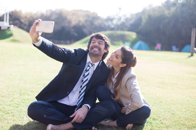 Compañeros de trabajo sonrientes haciéndose una foto sentados en el césped