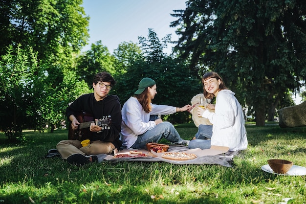 Compañía de hermosos jóvenes almorzando al aire libre. Concepto de comida rápida.