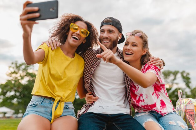 Compañía joven feliz con estilo colorido de amigos sentado en el parque