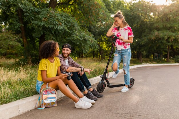 Compañía joven feliz de hablar amigos sonrientes sentados en el parque, hombres y mujeres que se divierten pasando tiempo juntos