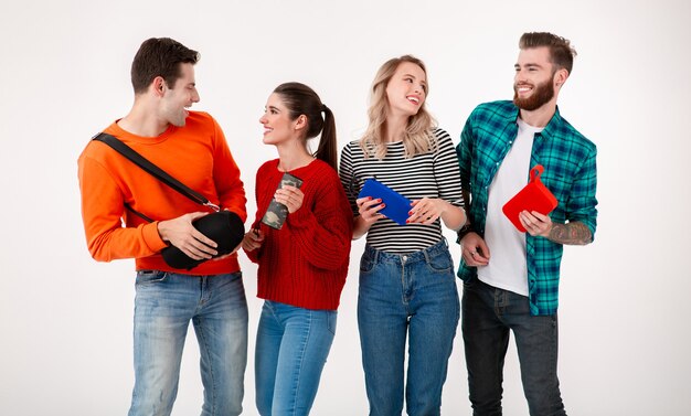 Compañía joven inconformista de amigos divirtiéndose juntos sonriendo escuchando música en altavoces inalámbricos