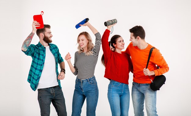 Compañía joven inconformista de amigos divirtiéndose juntos sonriendo escuchando música en altavoces inalámbricos