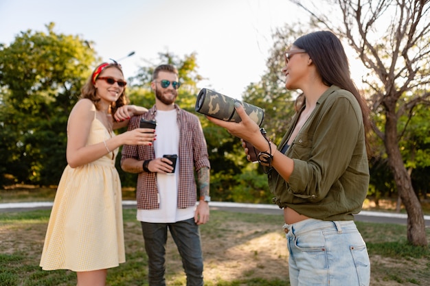 Compañía joven inconformista de amigos que se divierten juntos en el parque sonriendo escuchando música en el altavoz inalámbrico