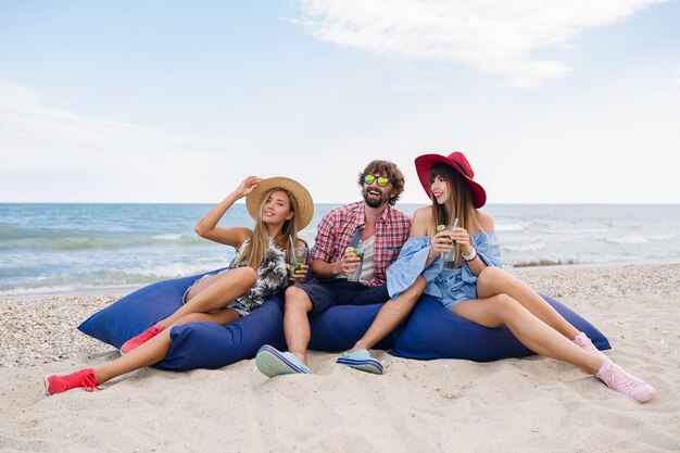 Compañía joven inconformista de amigos de vacaciones en el café de la playa, bebiendo un cóctel mojito, feliz positivo, estilo veraniego, sonriendo feliz, dos mujeres y un hombre divirtiéndose juntos, hablando, coqueteando, romance, tres