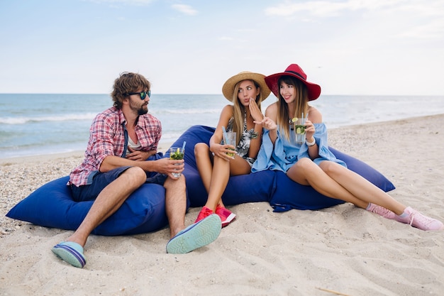 Compañía joven inconformista de amigos de vacaciones en el café de la playa, bebiendo cócteles mojito