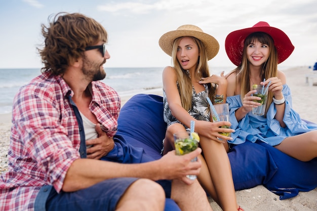 Compañía joven inconformista de amigos de vacaciones en el café de la playa, bebiendo cócteles mojito