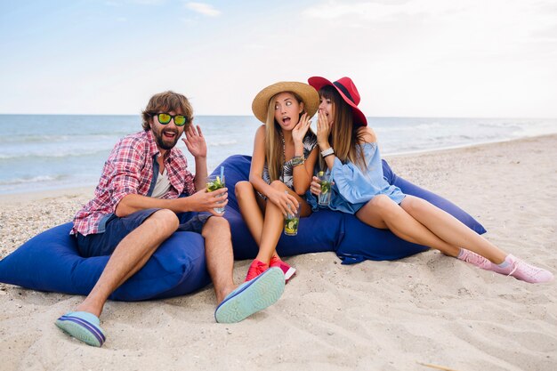 Compañía joven inconformista de amigos de vacaciones sentados en la playa en bolsas de frijoles