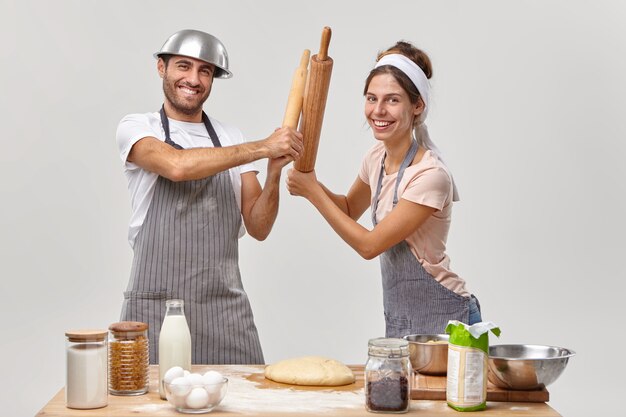 Los competidores profesionales de restaurantes tienen batalla con rodillos, participan en la batalla culinaria, miran con alegría, preparan comida sabrosa, prepárense para el fin de semana de fiesta. Pareja, cocina, juntos