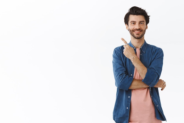 Foto gratuita complacido, confiado, apuesto, hombre barbudo con camiseta, apuntando a la esquina superior izquierda, sonriendo satisfecho y divertido, da consejos mostrando orgullosamente a un amigo dónde se esconden los regalos de navidad de la familia.