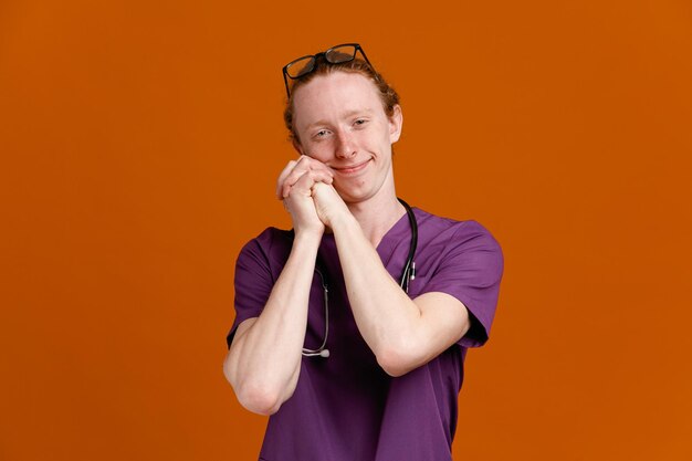 complacido tomados de la mano joven médico masculino vistiendo uniforme con estetoscopio aislado sobre fondo naranja