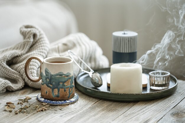 Composición acogedora con una taza de cerámica, velas y un elemento de punto.