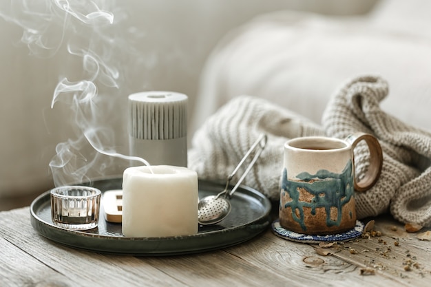 Composición acogedora con una taza de cerámica, velas y un elemento de punto.