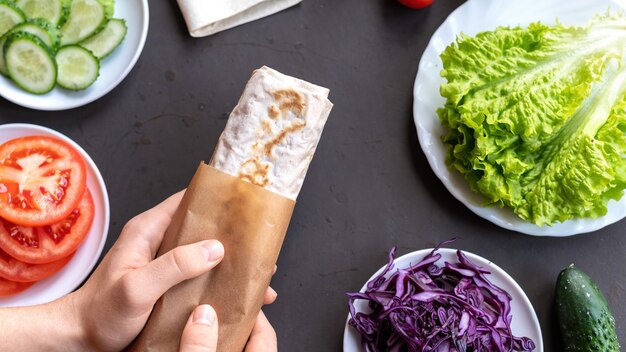 Composición de alimentos saludables. Verduras en platos y manos masculinas sosteniendo un rollo de pita