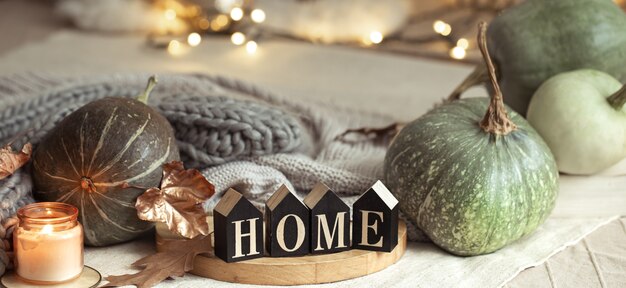 Composición ambiente hogareño de otoño en el interior con calabazas y letras de madera con las palabras casa sobre fondo borroso con bokeh. De cerca.