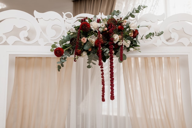 Composición en el arco de boda blanco hecho de eucalipto y flores de burdeos