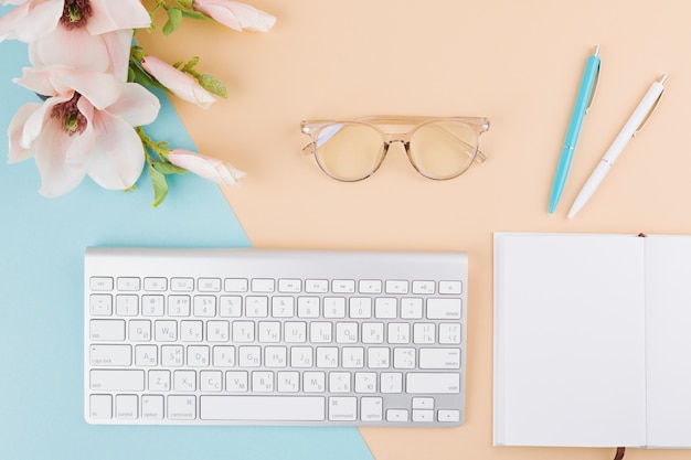 Composición de bloc de notas, teclado, lentes, flores y bolígrafos.