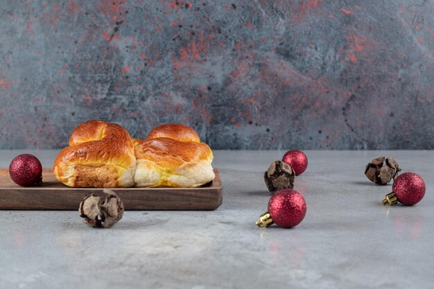 Composición de bolas navideñas y un bollo dulce sobre mesa de mármol.