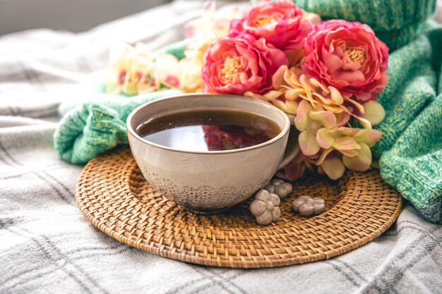 Composición casera con una taza de flores de té y un elemento de punto en la cama.