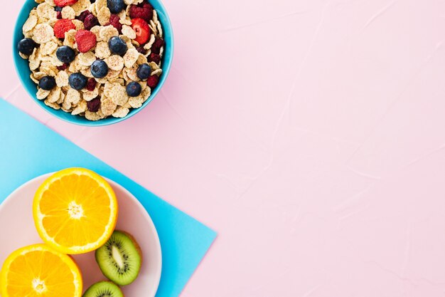 Composición de desayuno de verano. Cereales, frutas sobre fondo rosa pastel.