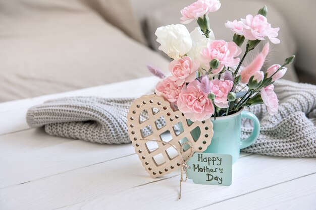 Una composición festiva con flores frescas en un jarrón, elementos decorativos y un deseo de un feliz día de la madre en una postal.