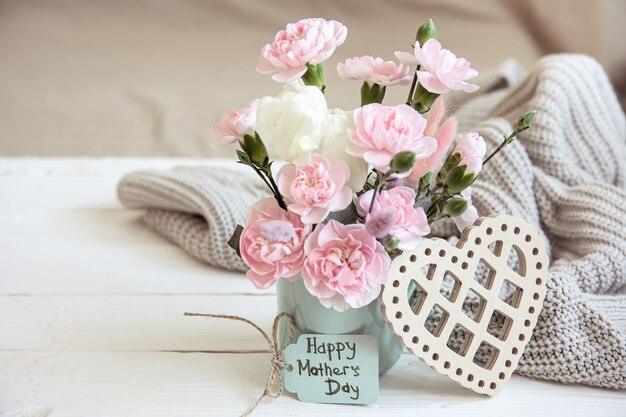 Una composición festiva con flores frescas en un jarrón, elementos decorativos y un deseo de un feliz día de la madre en la tarjeta.