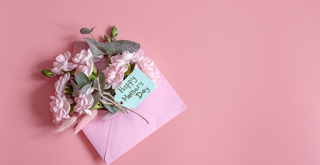 Composición festiva con un sobre con flores frescas y la inscripción Feliz Día de la Madre.