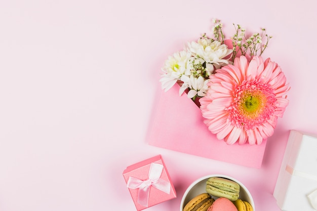 Foto gratuita composición de flores frescas en sobre cerca del presente y macarrones.