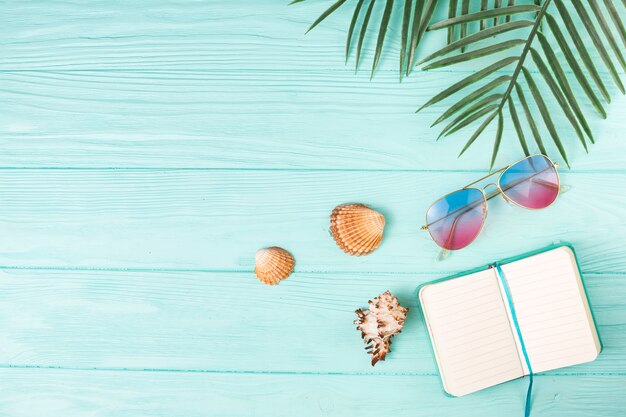 Composición de gafas de sol con cuaderno y hojas de palma.