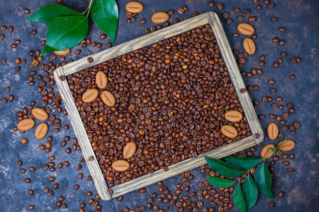Composición con granos de café tostados y galletas con forma de grano de café sobre una superficie de color marrón oscuro