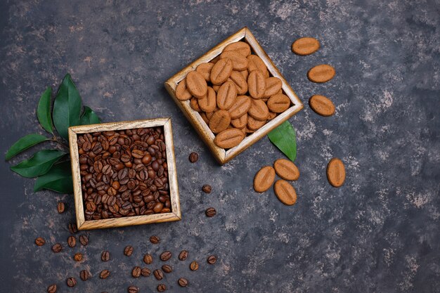 Composición con granos de café tostados y galletas con forma de grano de café sobre una superficie de color marrón oscuro