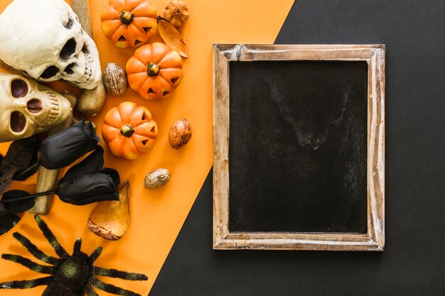 Composición de halloween con pizarra, cráneos y araña