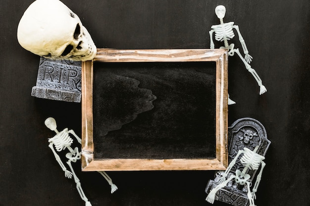 Composición de halloween con pizarra, esqueletos y cráneo