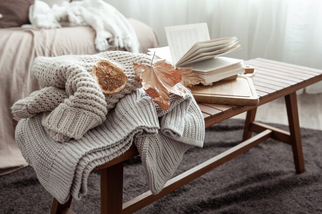 Una composición hogareña acogedora con un suéter de punto, un libro y hojas en el interior de la habitación.
