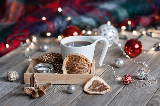 Composición de invierno acogedor con una taza de bebida caliente, detalles decorativos y bolas de Navidad sobre un fondo borroso con bokeh.