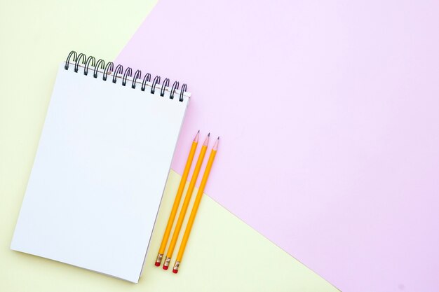 composición de lay plana con cuaderno vacío con lápices sobre fondo rosa y amarillo