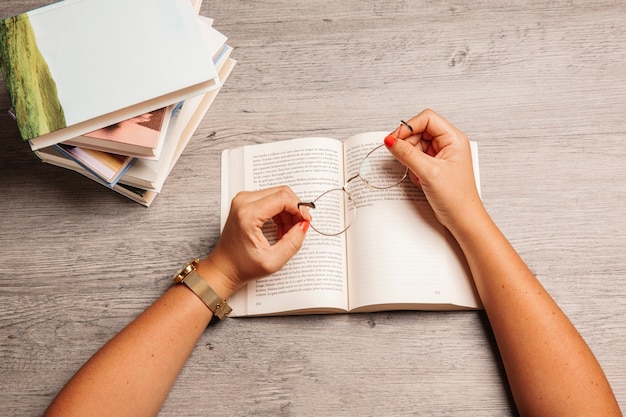 Composición de literatura con manos sujetando gafas de lectura