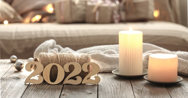 Composición de Navidad casera con números decorativos de madera 2022, velas y detalles de decoración sobre un fondo interior de habitación borrosa.