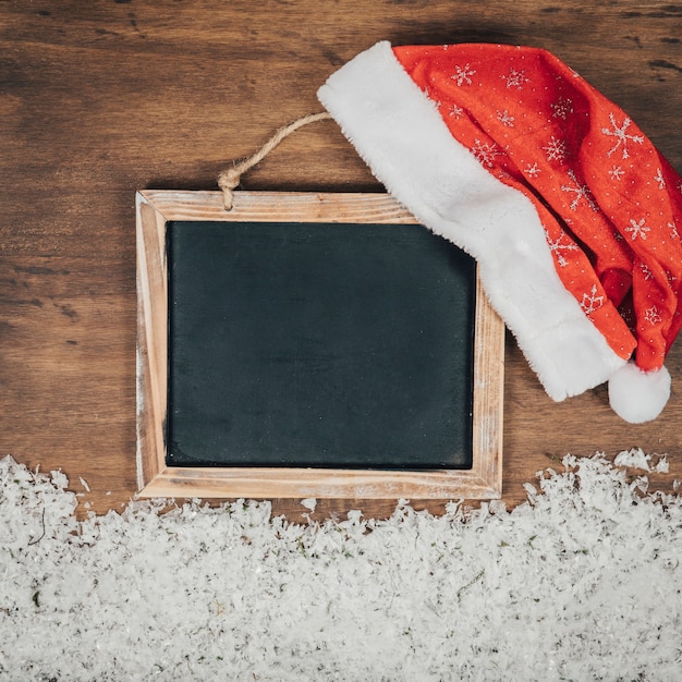 Foto gratuita composición de navidad con gorro en pizarra y nieve