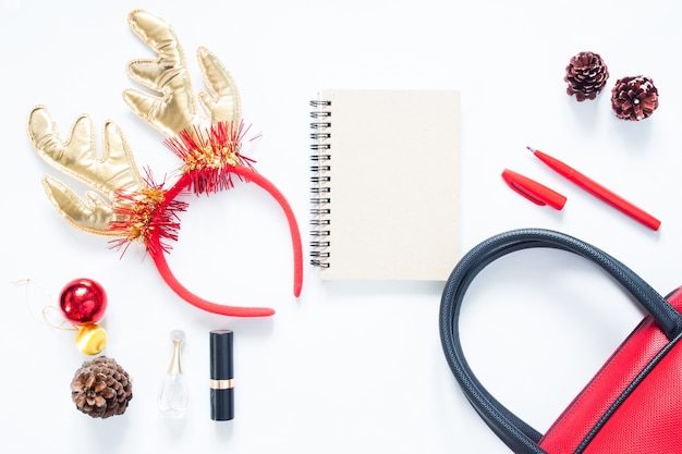 Composición de Navidad. Moda de Navidad para niña, cosméticos, bolsa, conos de pino, bloc de notas y lápiz rojo con copia espacio. Vista plana