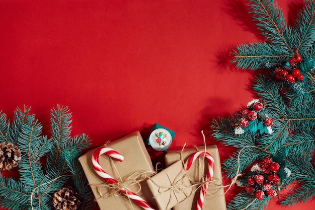 Composición navideña de conos de pino ramas de abeto y pila de cajas de regalo sobre fondo rojo.