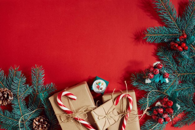 Composición navideña de conos de pino ramas de abeto y pila de cajas de regalo sobre fondo rojo.