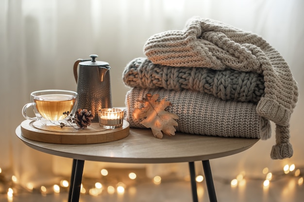 Composición de otoño en casa con té y suéteres de punto en el interior de la habitación, sobre un fondo borroso con una guirnalda.