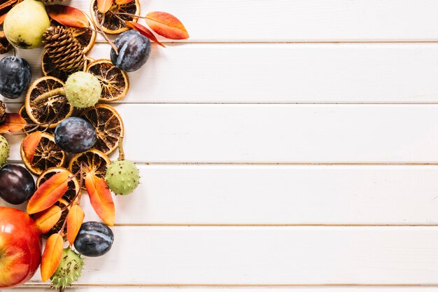 Composición de otoño con frutas y hojas sobre fondo blanco de madera