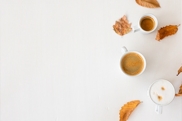 Composición de otoño con tazas de café y hojas sobre un fondo blanco.