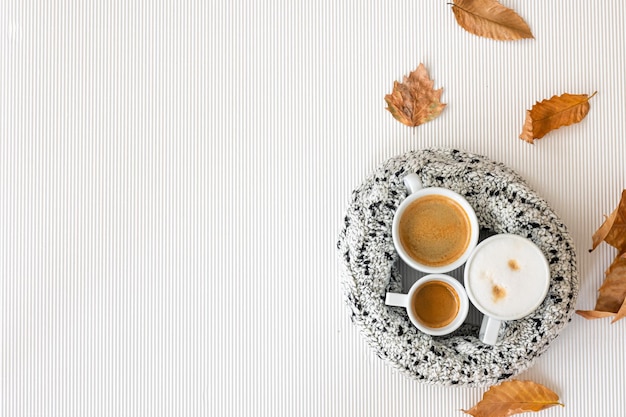 Composición de otoño con tazas de café y hojas sobre un fondo blanco.