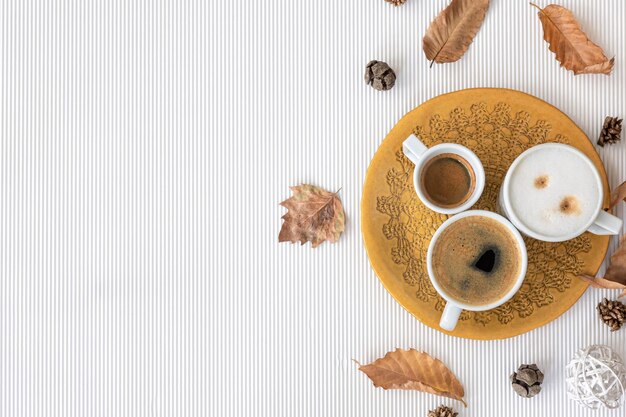 Composición de otoño con tazas de café y hojas sobre un fondo blanco.