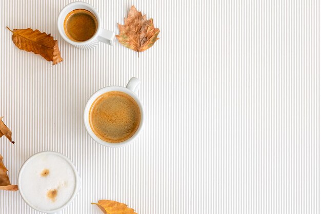 Composición de otoño con tazas de café y hojas sobre un fondo blanco.