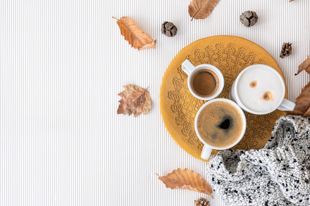 Composición de otoño con tazas de café y hojas sobre un fondo blanco.