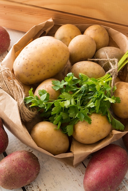 Composición de papas crudas en bolsa de papel sobre fondo de madera